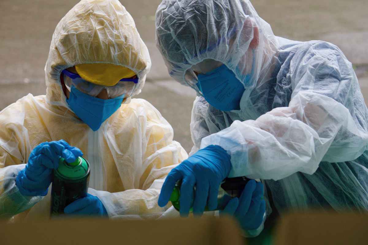 Zwei Kinder in kompletter Schutzausrüstung mit Overall, Handschuhe, Schutzbrille und Maske sprayen.