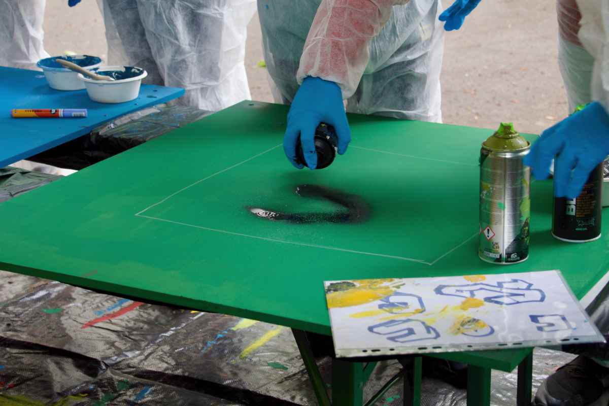 Ein Kind sprüht mit schwarzer Farbe auf eine grüne Holzplatte.