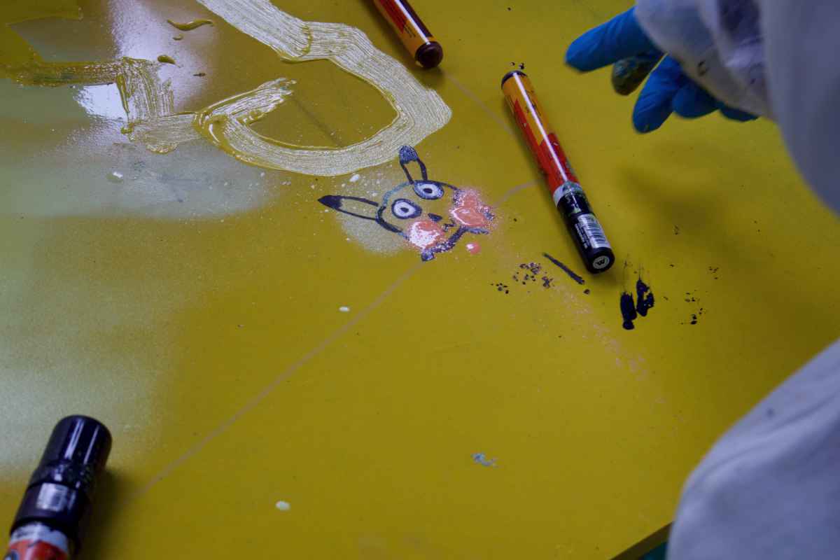 Eine Art gemalter Hase oder Minion ist auf einer gelben Holzplatte zu sehen. Ein paar schwarze Marker liegen daneben.