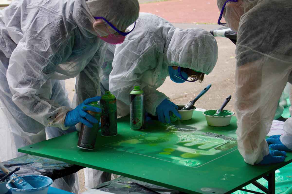 Drei Kinder arbeiten gemeinsam an einer grünen Holzplatte. Mit grüner Sprühfarbe.