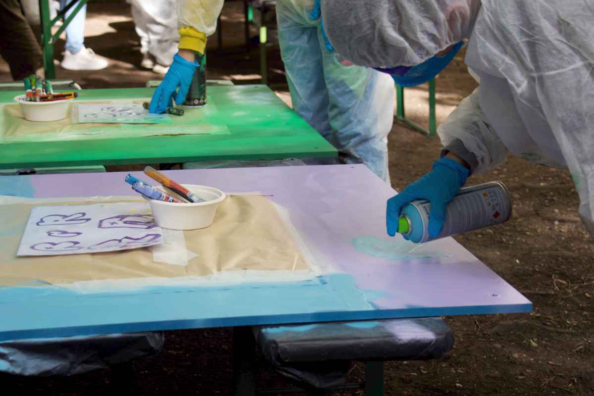 Ein hellblaues R wird auf eine rosafarbige Holplatte gesprüht.